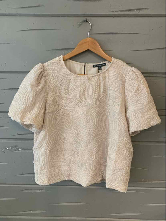Beige textured short-sleeve blouse with puffed sleeves and round neckline hanging on wooden hanger.