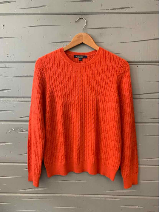 Bright orange cable-knit wool sweater with crew neck and long sleeves on wooden hanger.