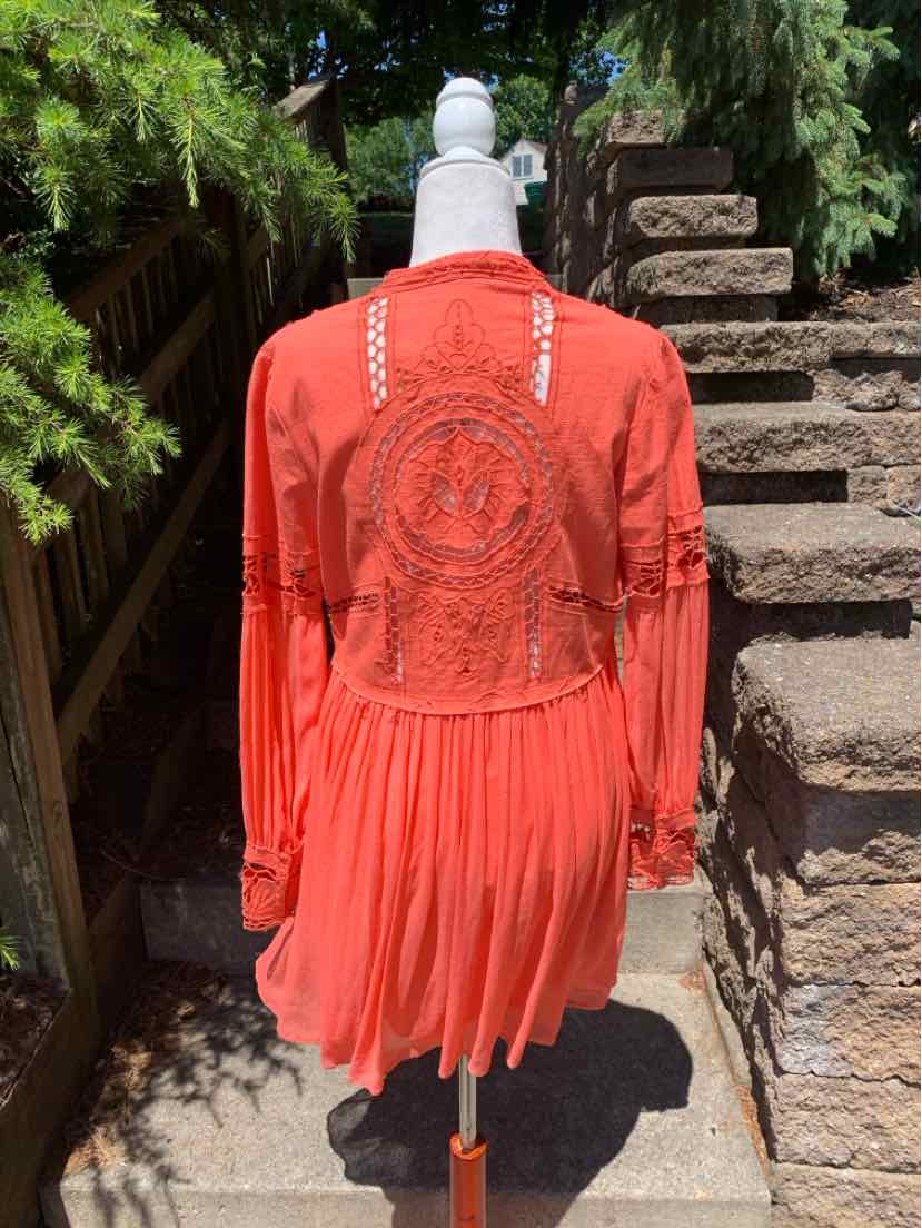Coral long-sleeve dress with pleated skirt and intricate circular lace detail on back, lightweight fabric.