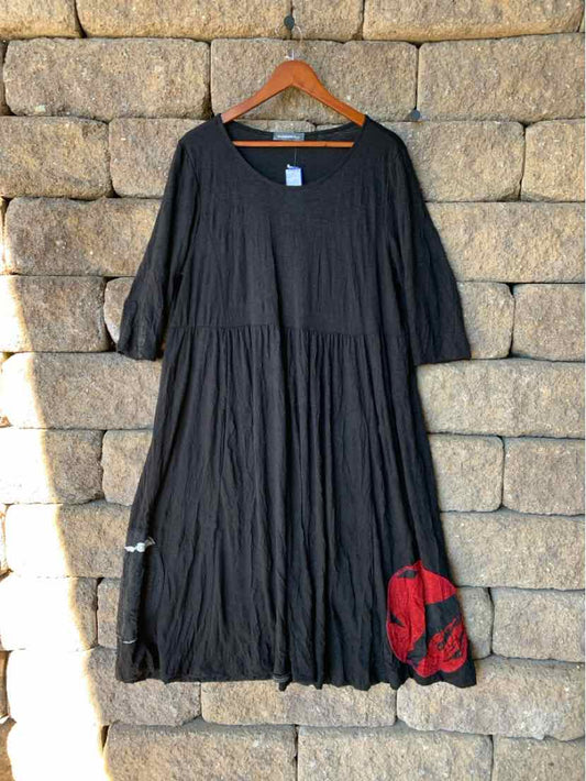 Black Alembika dress with a round neckline, elbow-length sleeves, gathered waist, and red floral detail near the hem.