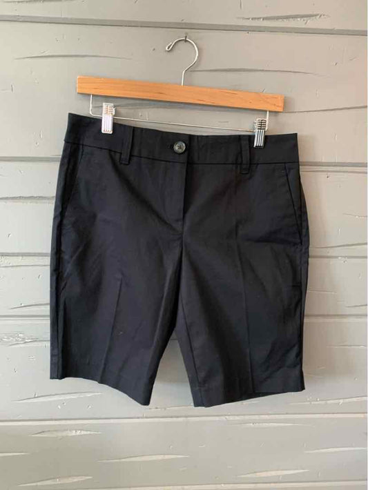 Black tailored knee-length shorts with front button and zip closure on wooden hanger.