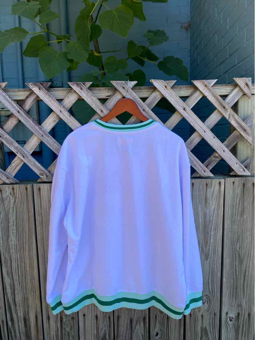 White long-sleeve shirt with green and blue striped trim on cuffs and hem, hanging on wooden hanger outdoors.