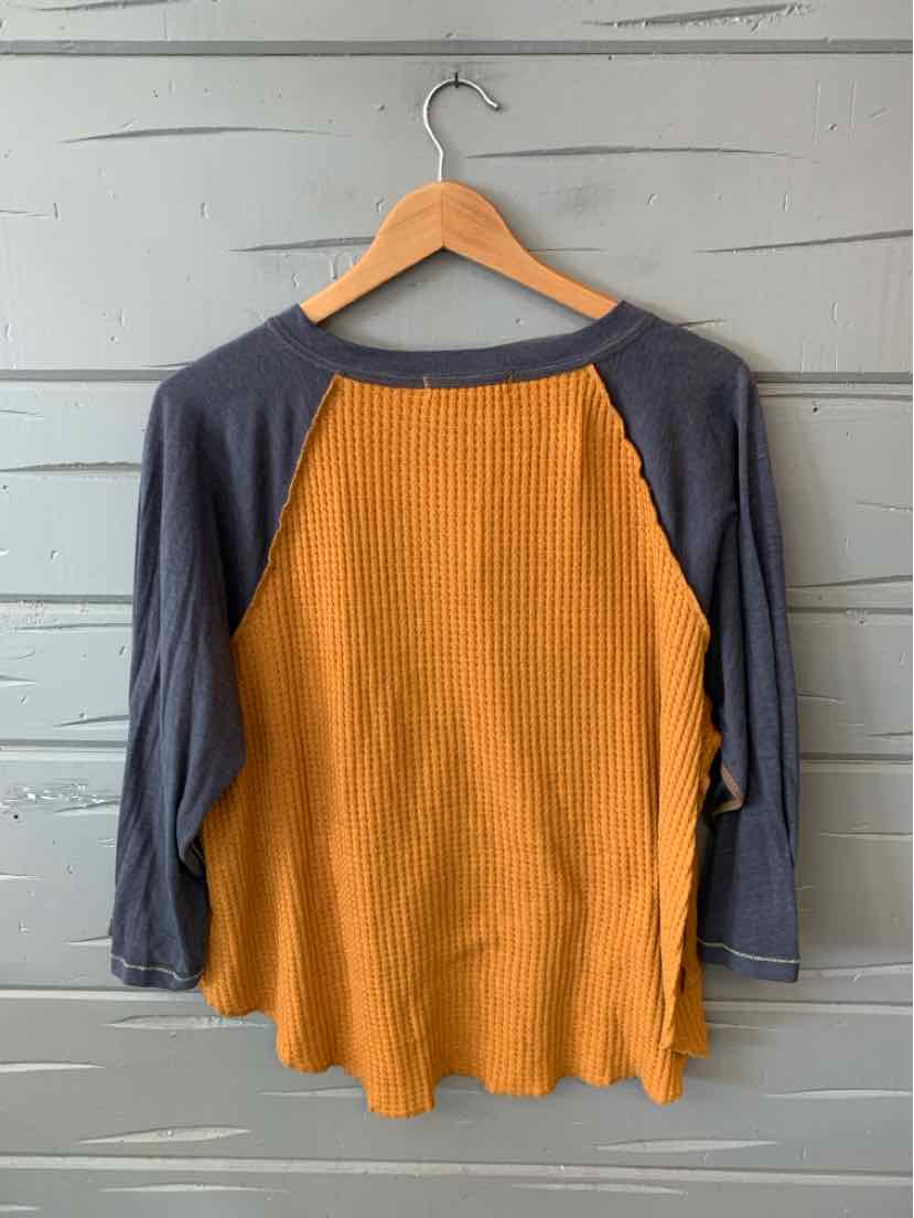Long-sleeve waffle knit shirt with orange body and dark gray raglan sleeves on wooden hanger.
