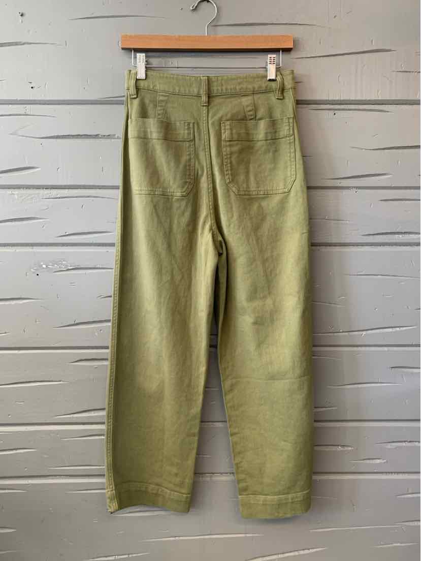 Olive green straight-leg pants with back pockets hanging on wooden hanger against gray wall.