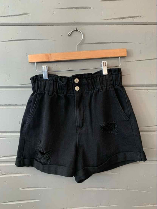 Black high-waisted denim shorts with distressed details and folded hems on wooden hanger.