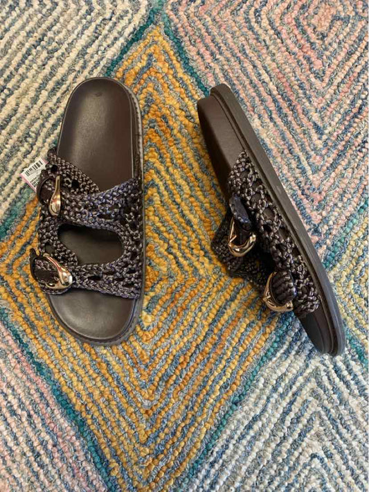 Black woven double-strap slide sandals with adjustable buckles, size 10, on textured multicolor rug.