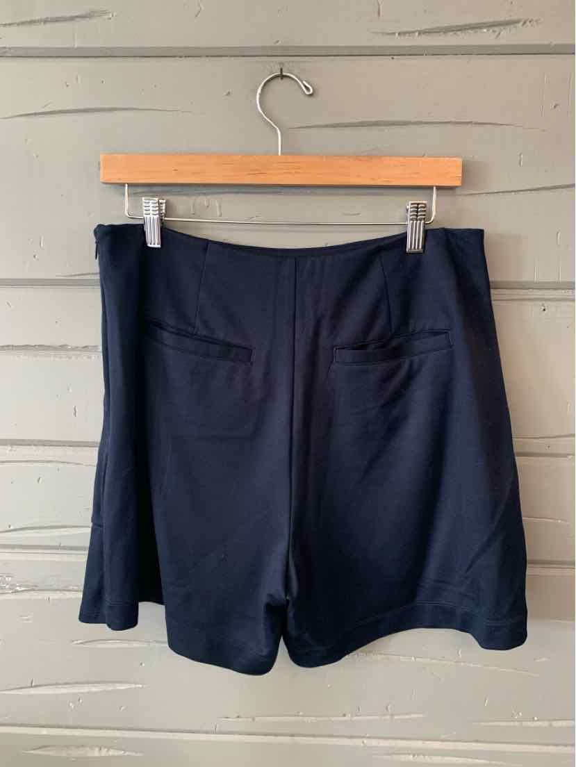 Black tailored shorts with back welt pockets hanging on wooden hanger against gray wooden wall.