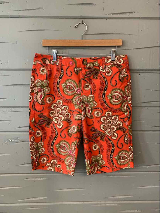 Orange paisley-patterned shorts with front pockets and belt loops, size 8, hanging on wooden hanger.