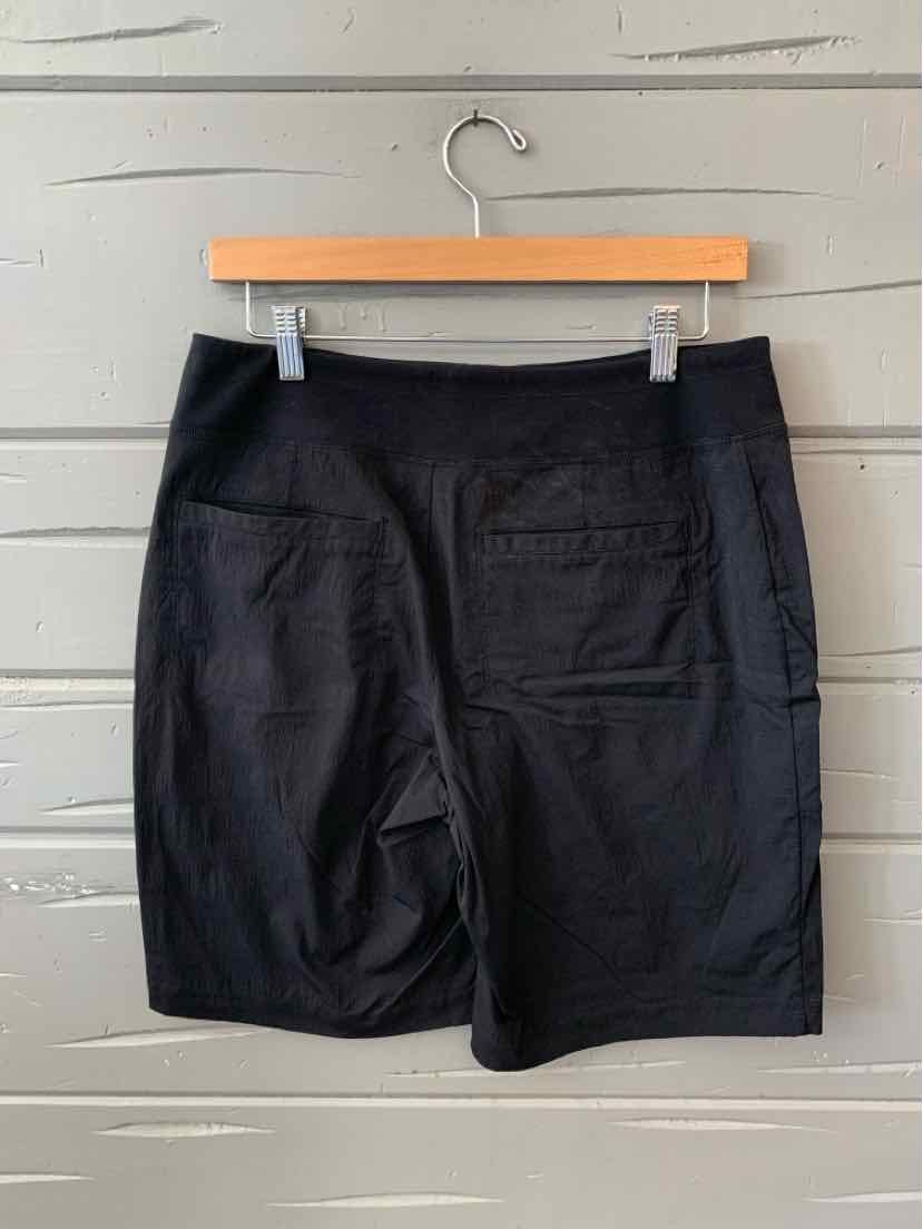 Black mid-length athletic shorts with flat waistband and rear patch pockets, hanging on wooden hanger.