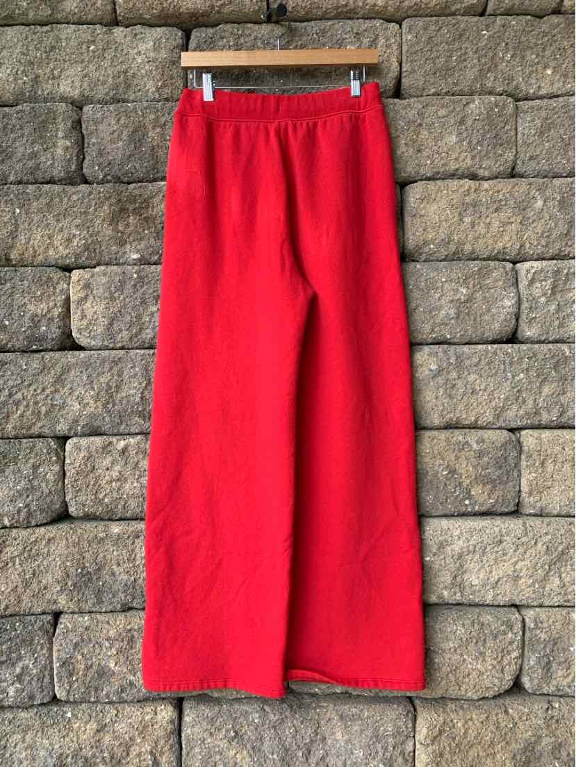 Bright red wide-leg pants with elastic waistband hanging against a stone wall background.