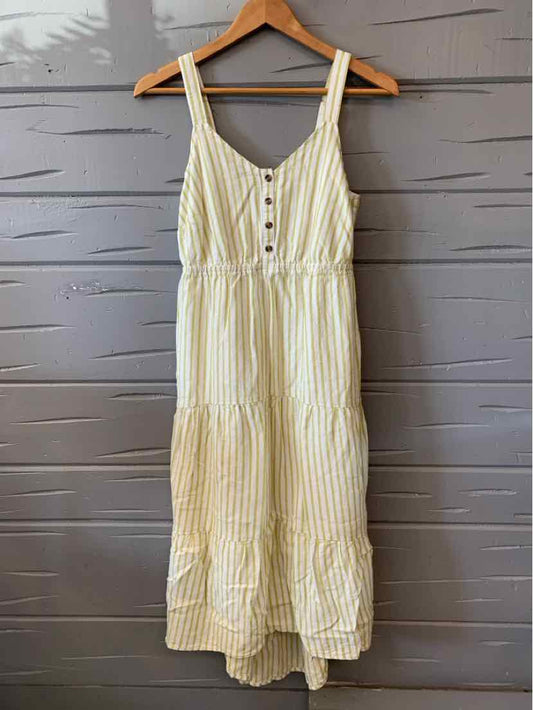 Green and white vertical striped sleeveless dress with button-down front and tiered hem hanging on wooden hanger.