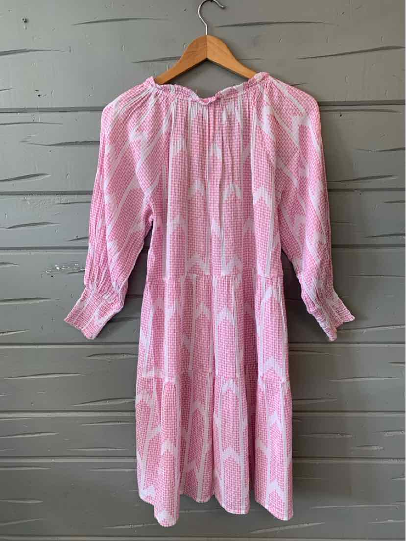 Pink long-sleeve dress with geometric white pattern and gathered neckline on wooden hanger.