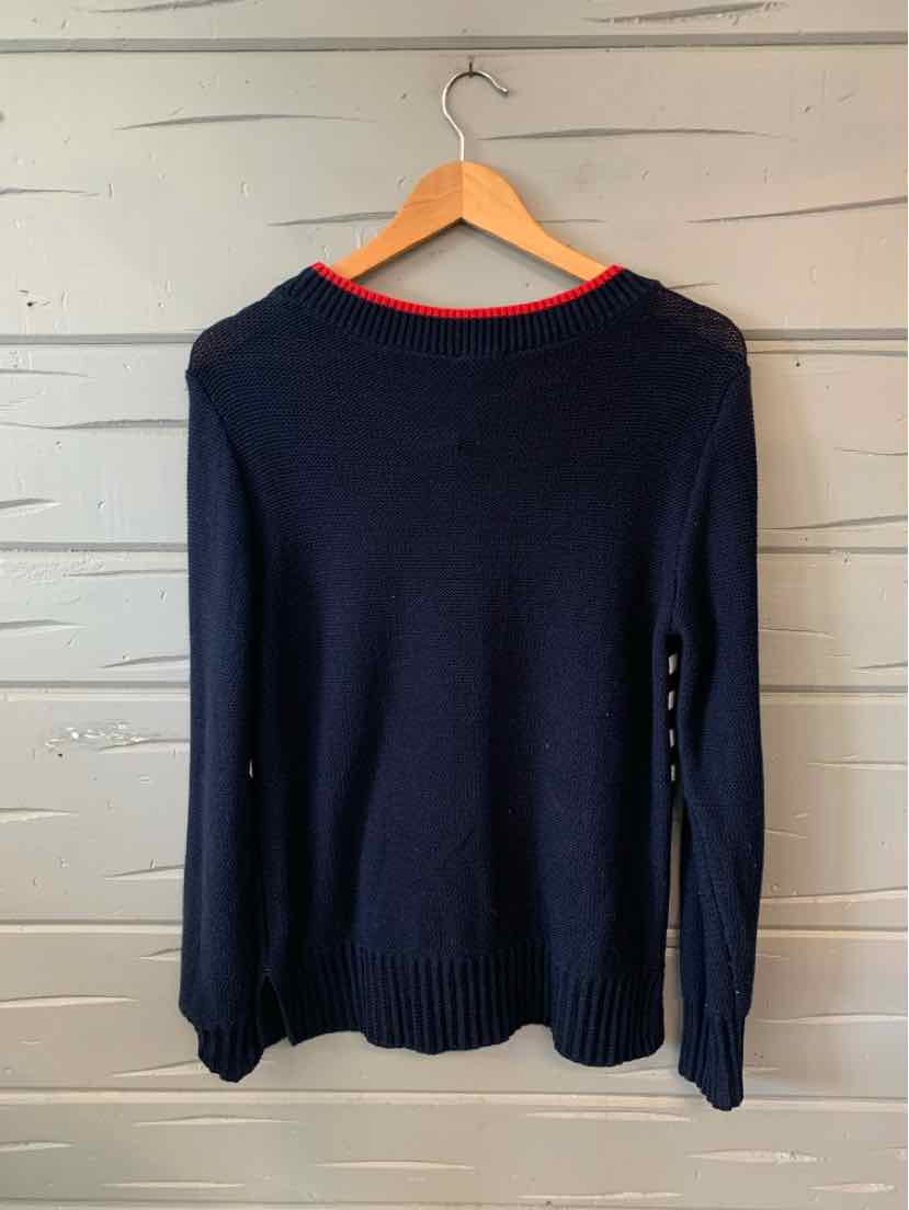 Navy blue long-sleeve sweater with a red trim around the neckline on a wooden hanger against a white wooden background.