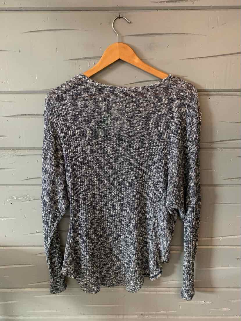 Gray and black marled knit sweater with long sleeves and relaxed fit hanging on wooden hanger.