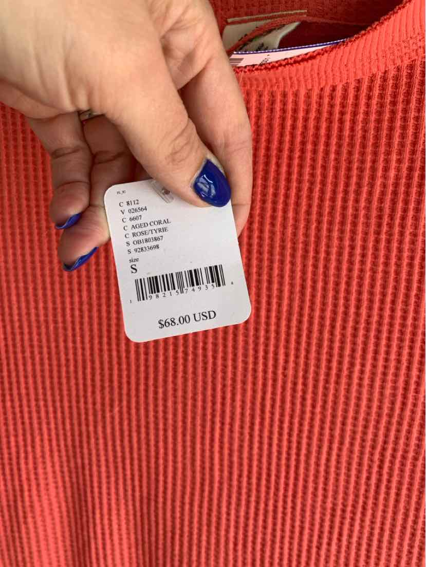 Hand holding white price tag on orange ribbed knit fabric showing $48.00 USD price.