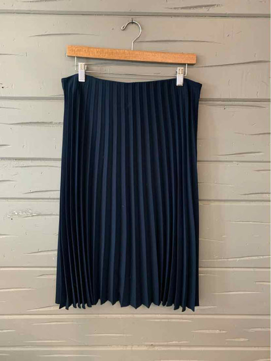 Navy blue pleated midi skirt with a high waist hanging on wooden hanger against gray wooden wall.