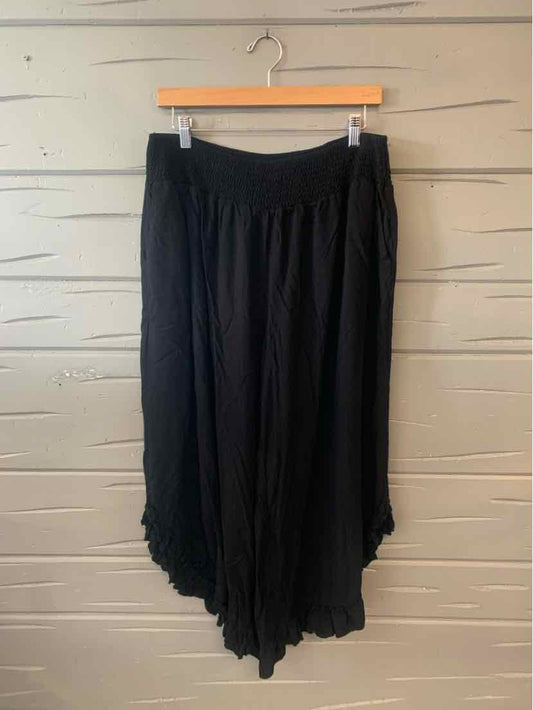 Black wide-leg flowy pants with elastic waistband and asymmetrical hem hanging on wooden hanger.