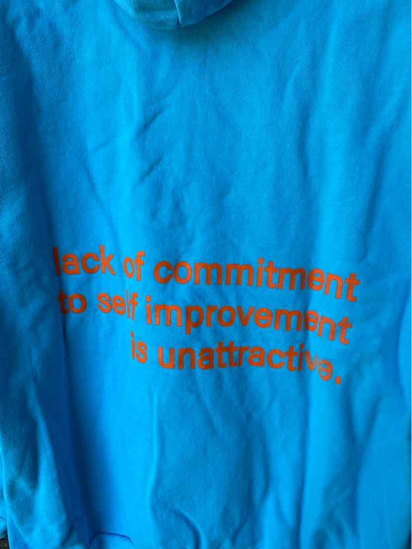 Bright blue fabric with bold orange text reading "lack of commitment to self improvement is unattractive" printed on it.