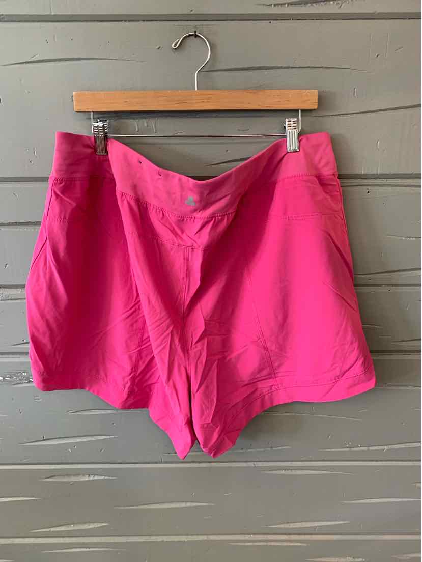 Bright pink women's shorts with front buttons and side pockets hanging on wood hanger against gray wall.