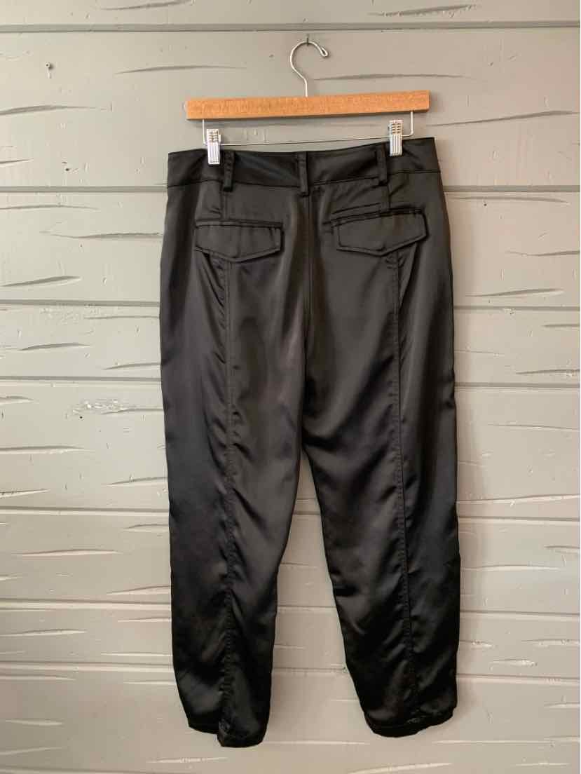 Black tapered pants with elastic cuffs and two back flap pockets hanging on wooden hanger.