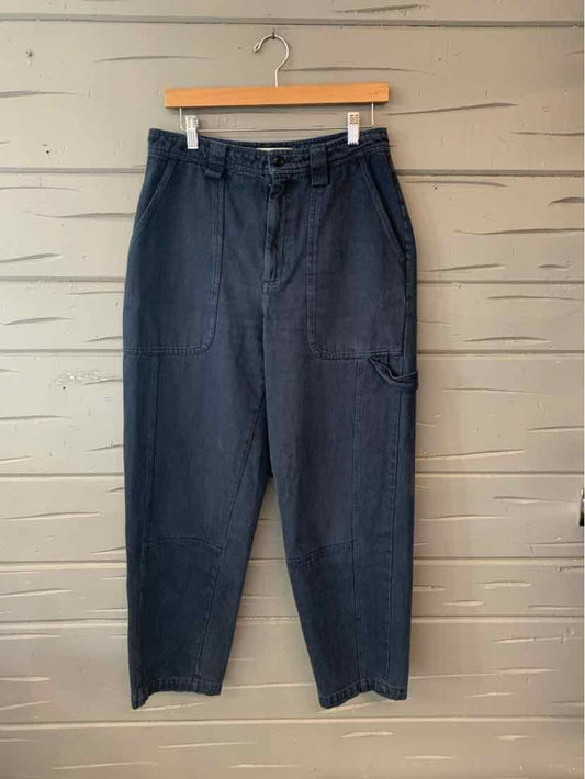 Black high-waisted trousers with front pleats and side pockets hanging on wooden hanger.