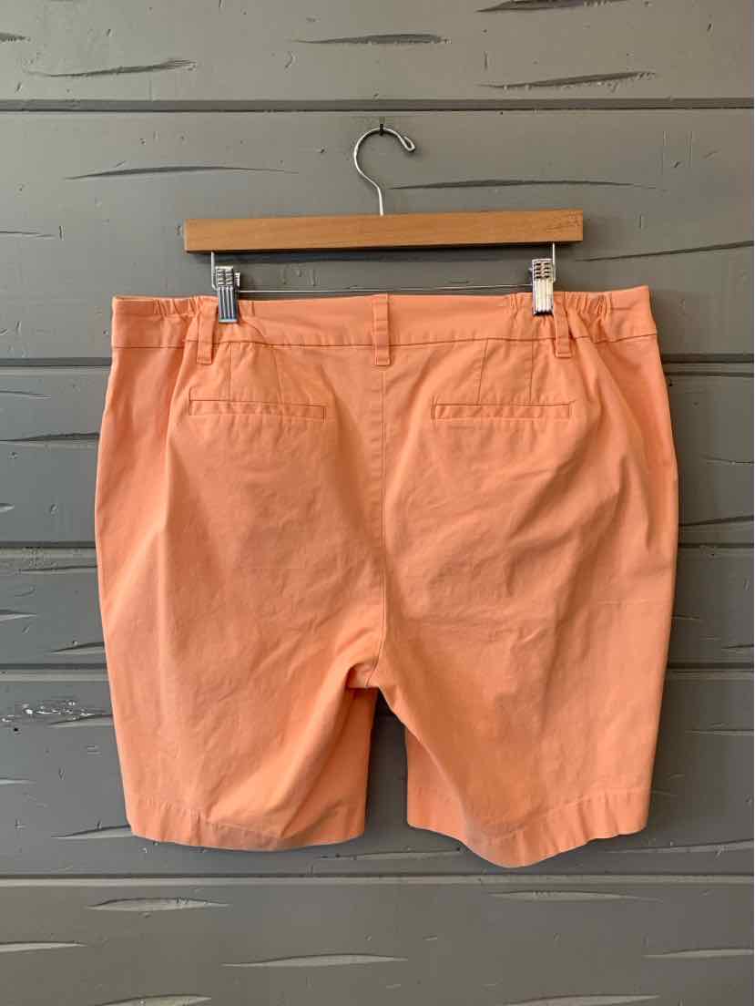 Salmon pink tailored shorts with back welt pockets on wooden hanger against gray wall.