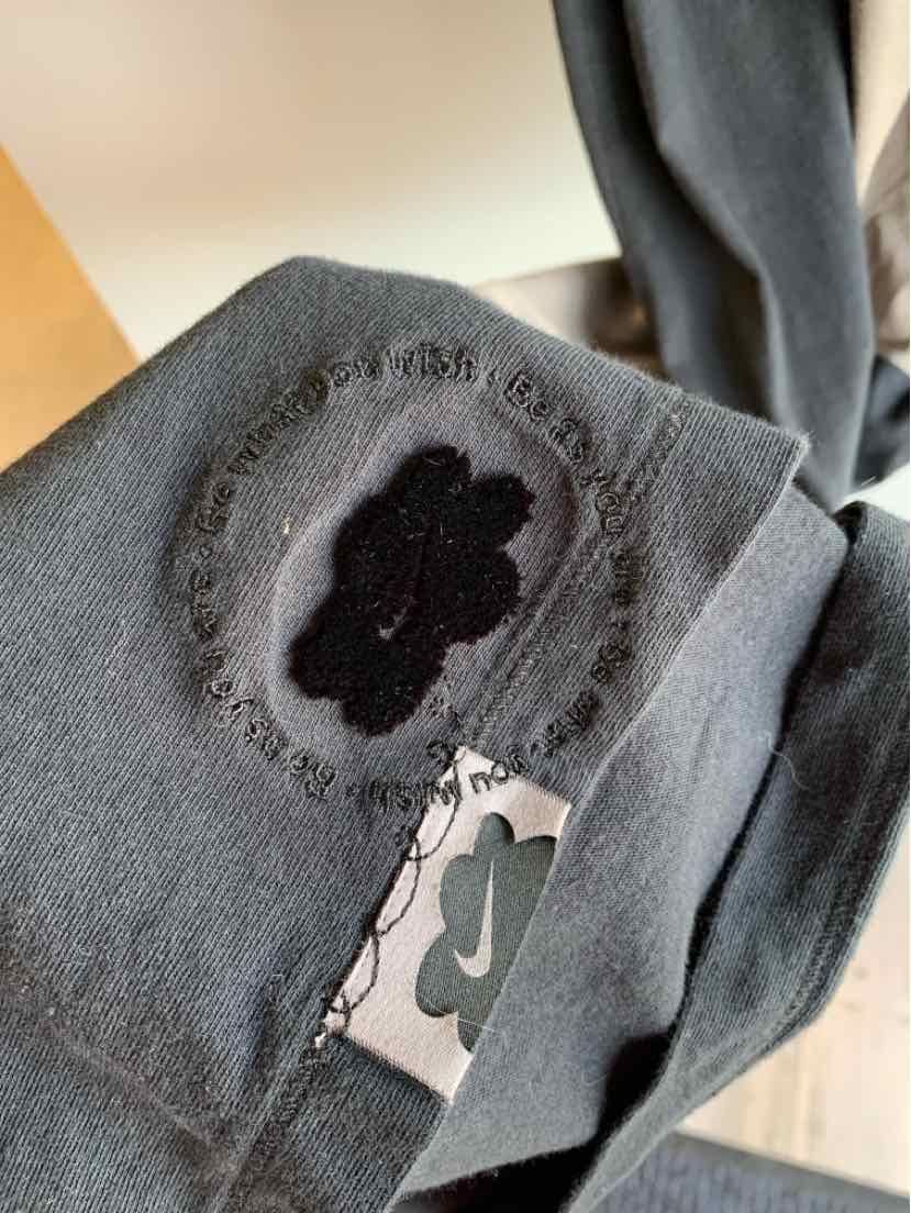 Dark gray Nike garment with black embroidered floral logo and a white tag featuring a black clover design.