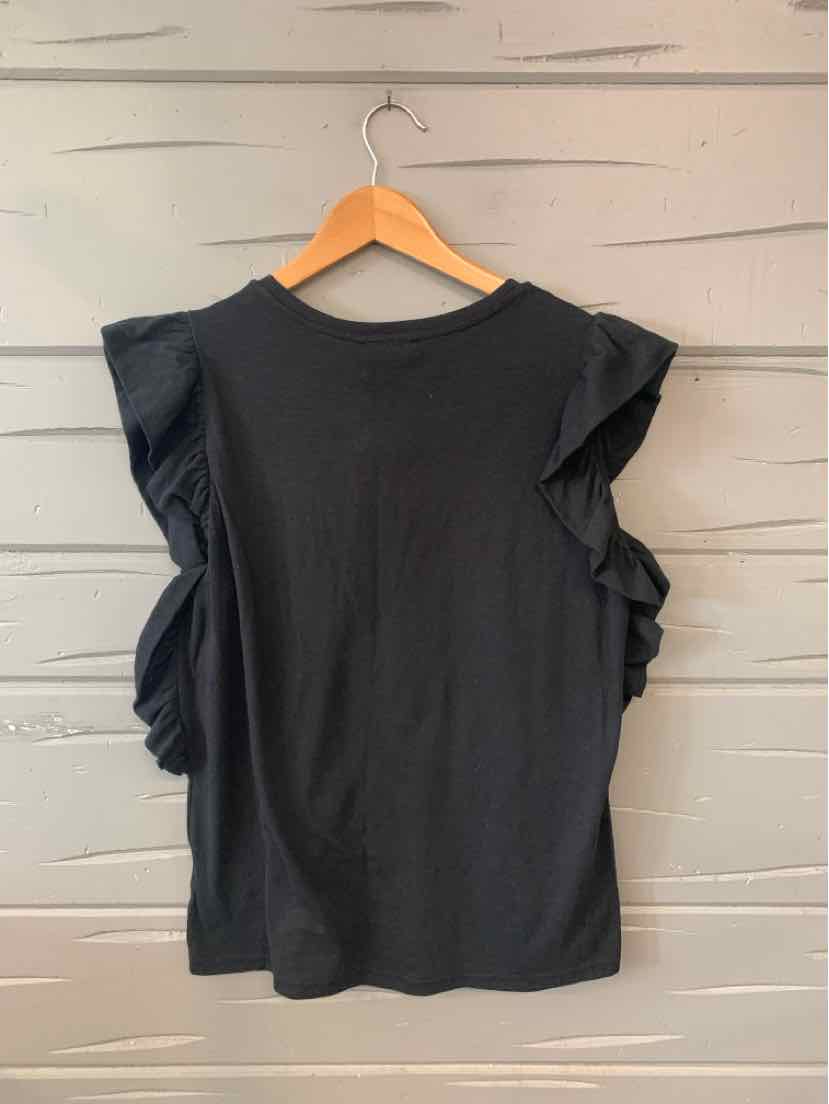 Black sleeveless top with ruffled shoulders hanging on wooden hanger against gray wooden wall.