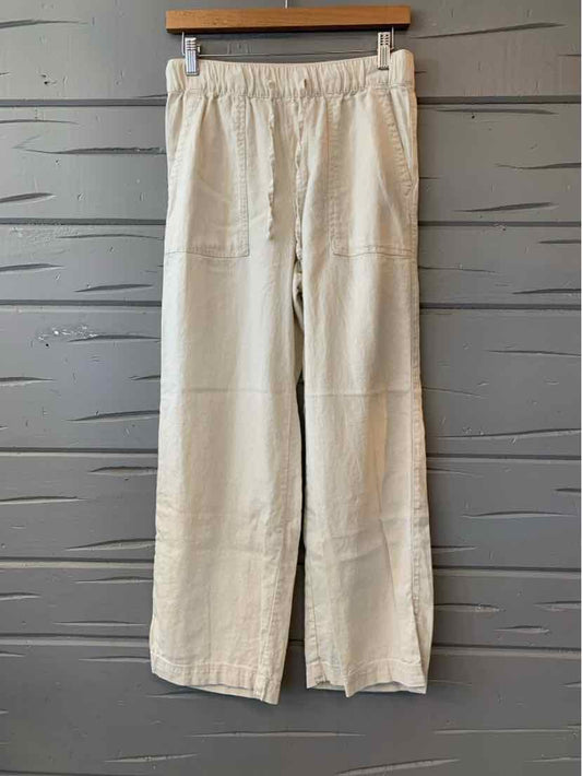 Light beige wide-leg pants with elastic waistband and visible front seams hanging on wooden hanger against textured gray wall.
