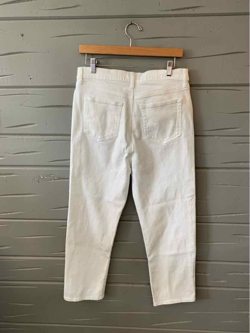 White denim cropped pants with back pockets and belt loops hanging on wooden hanger.