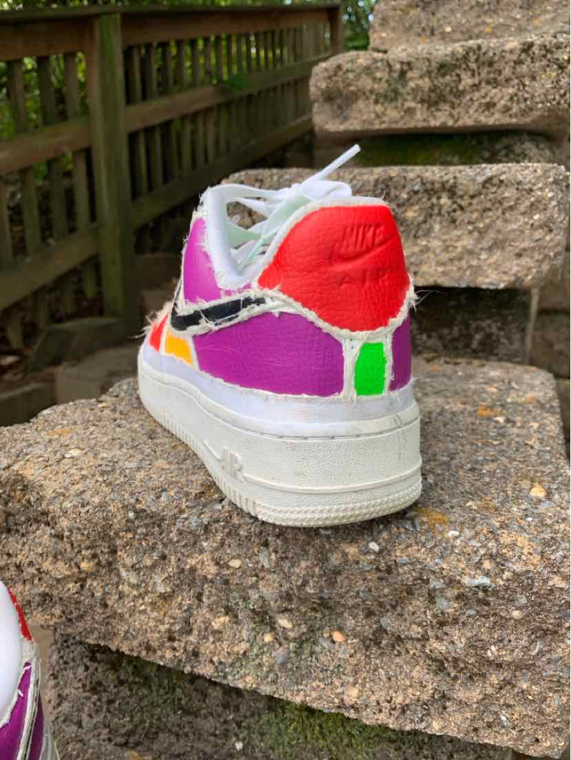 White Nike low-top sneaker with bright red heel, purple and green color panels, and white laces and sole.