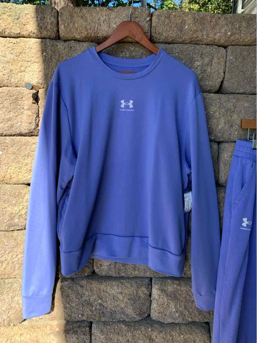 Blue Under Armour crewneck sweatshirt with long sleeves and a small white chest logo, hanging on a wooden hanger.