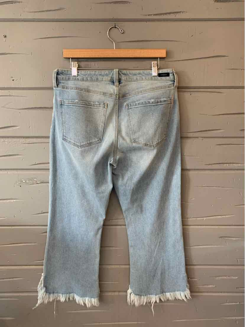 Light blue denim jeans with a relaxed fit, frayed hems, and two back pockets hanging on a wooden hanger against a textured.