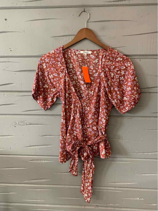 Rust-colored floral wrap blouse with puff sleeves and waist tie on wooden hanger.