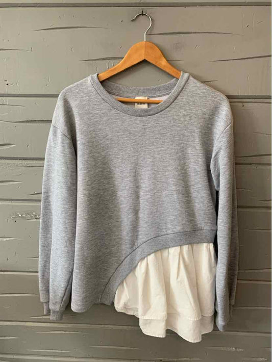 Gray long-sleeve sweatshirt with rounded neckline and attached white asymmetrical ruffle hem.