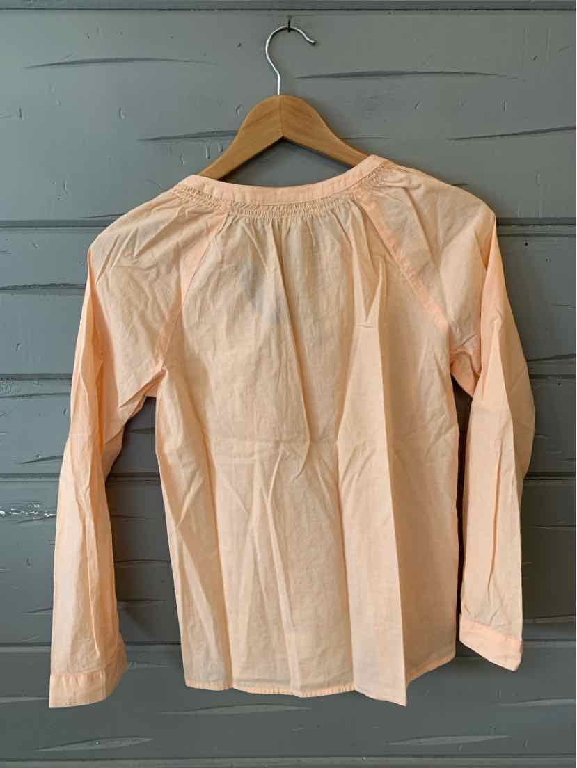 Light peach long-sleeve blouse with gathered neckline and relaxed fit on wooden hanger.