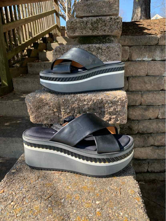 Black leather platform sandals with thick cross straps and striped white and black sole, size 40.5.