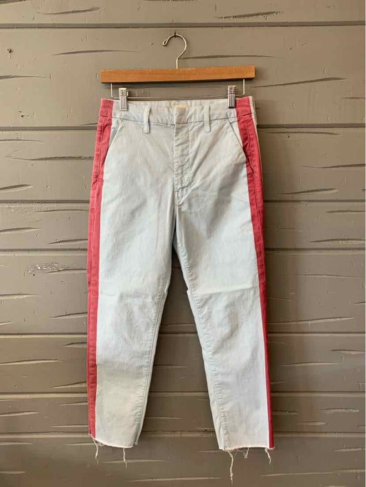 White high-waisted jeans with slim fit and red side stripes hanging on wooden hanger against gray wooden wall.