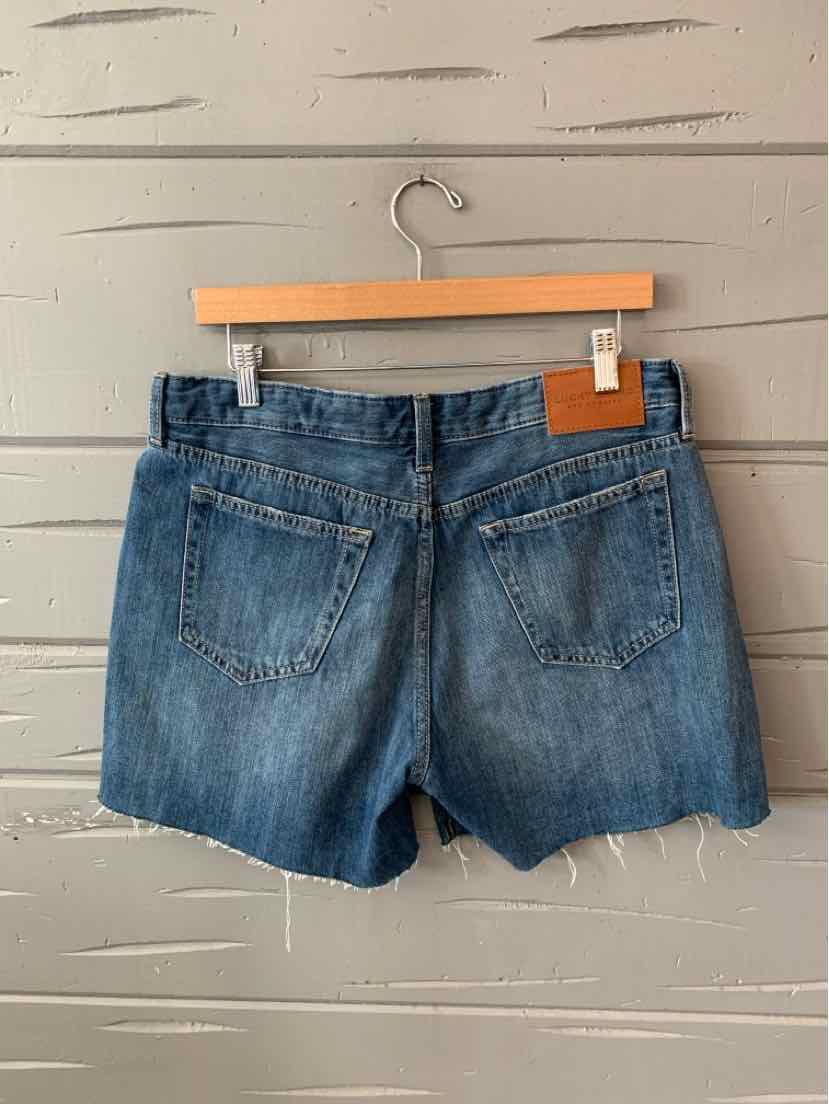 Blue denim shorts with frayed hems and back patch pockets hanging on wooden hanger.