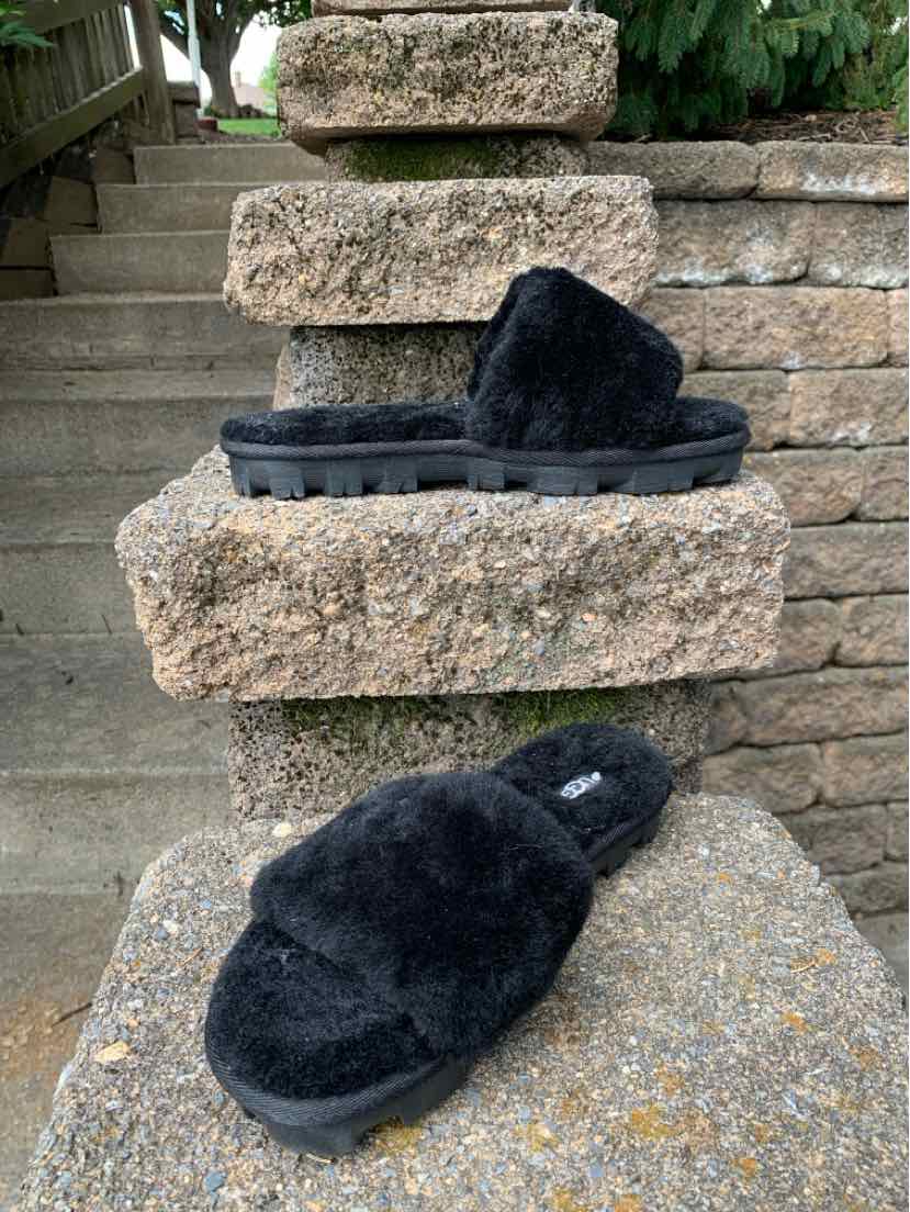 Black plush sherpa UGG slide sandals with thick textured soles and open toes.