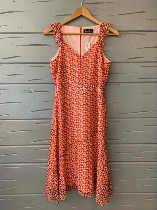 Orange sleeveless dress with white polka dots and ruffled shoulder straps on wooden hanger.