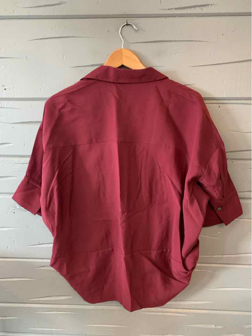 Solid burgundy short-sleeve blouse with relaxed fit and classic collar hanging on wooden hanger.