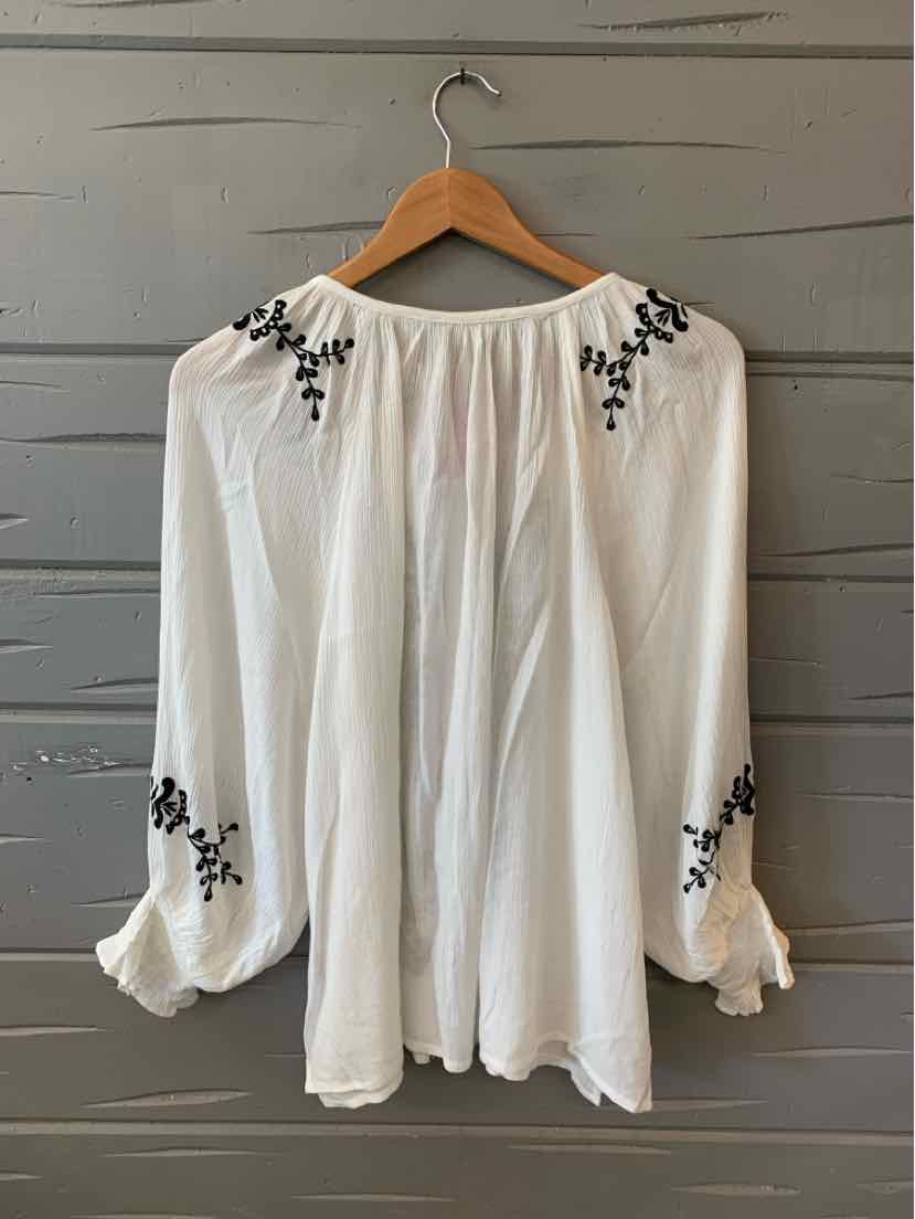 White long-sleeve blouse with black floral embroidery on shoulders and sleeves, loose fit, gathered neckline, and ruffled.
