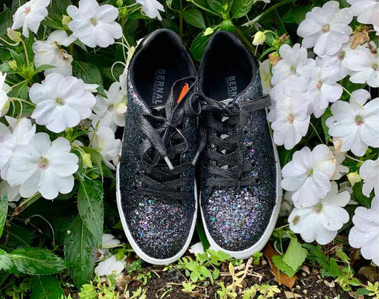 Black low-top sneakers with sparkling glitter on the toe and sides, white soles, and black laces.