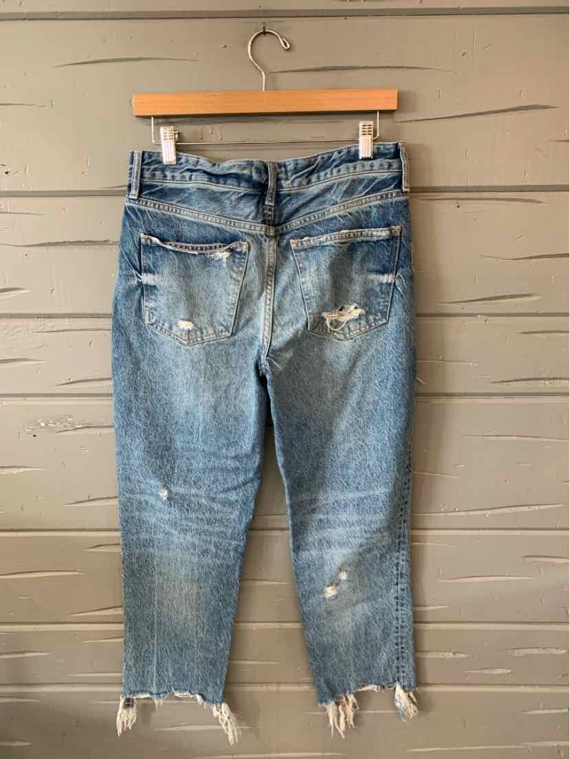 Light blue distressed denim jeans with frayed hems and back pockets hanging on a wooden hanger.