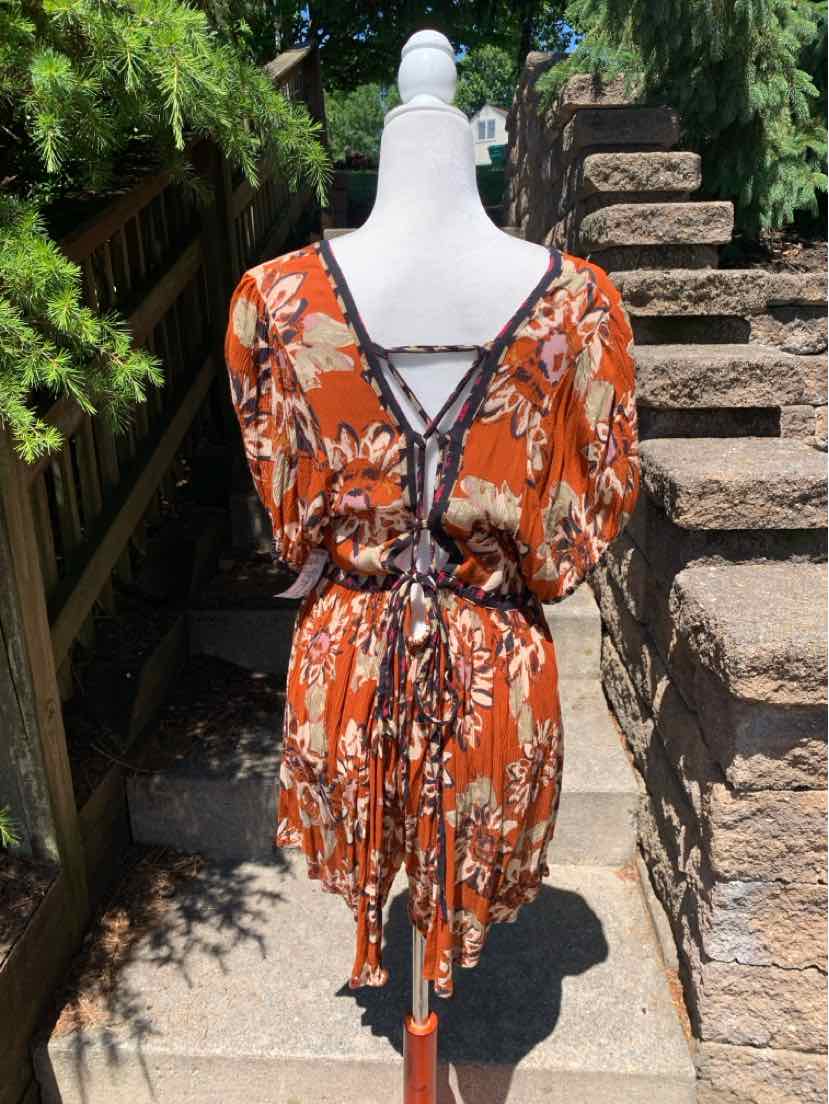 Rust-orange floral patterned dress with black lace trim and cinched waist tie on mannequin.