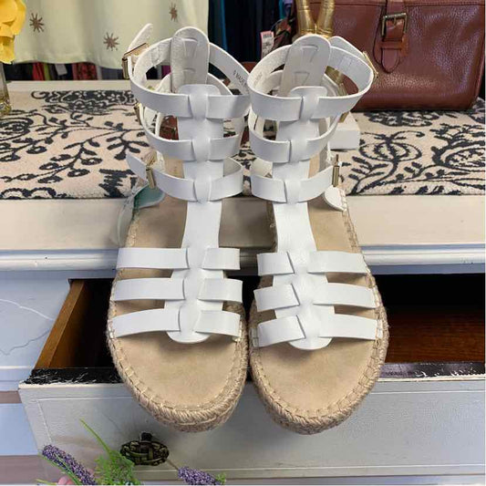 White gladiator-style sandals with multiple straps and ankle buckle closures on woven soles.