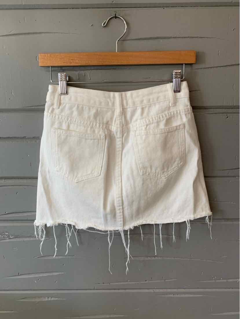 White denim mini skirt with frayed hem and back pockets hanging on wooden hanger.