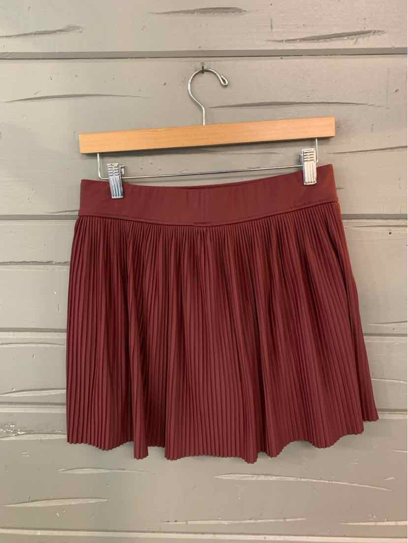Burgundy pleated skirt with wide elastic waistband hanging on wooden hanger.