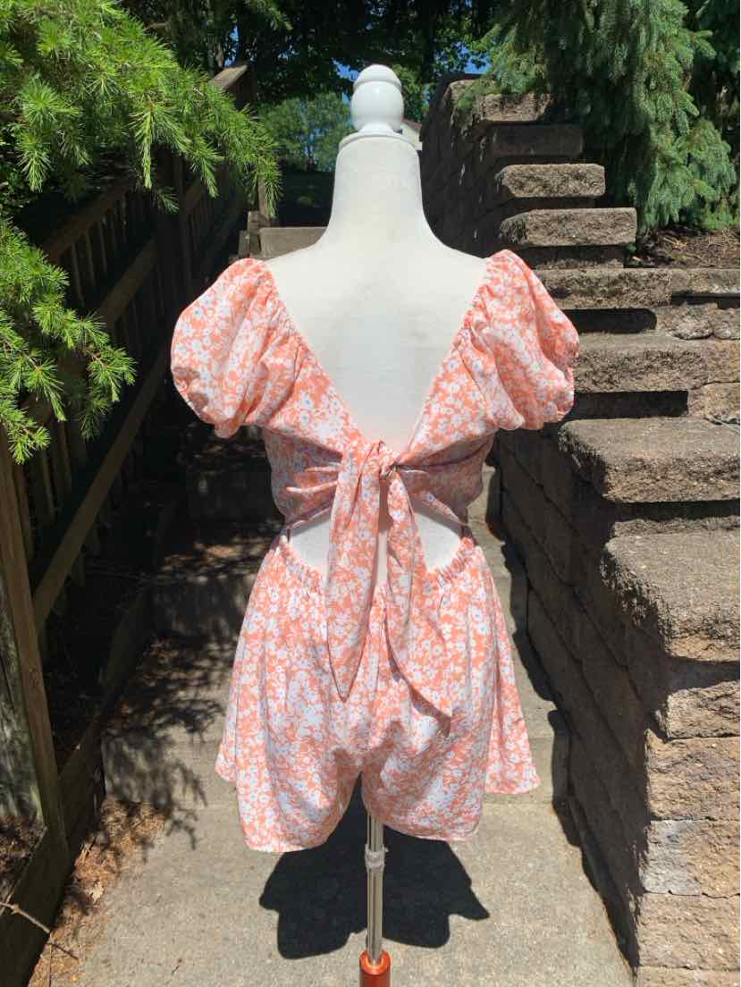 Light pink floral romper with puff sleeves, open back, and tie detail at waist.